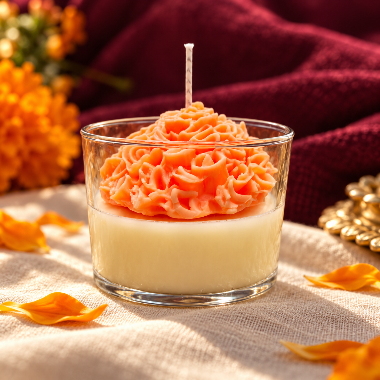 Vela artesanal Flor de Cempasúchil naranja de 170 gramos, sobre lino marfil y fondo vino.